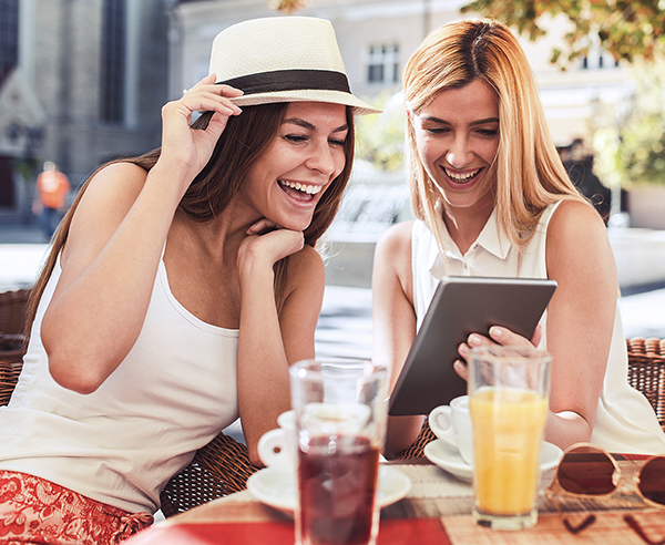 Two young women looking at device at lunch in city